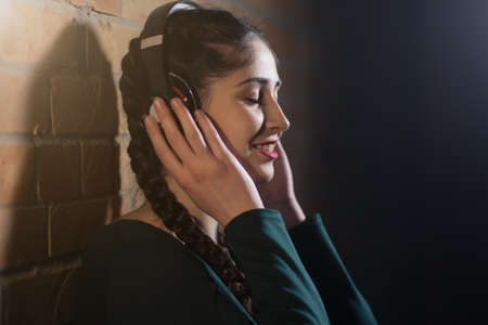 Woman in earphones listen music at brick wall in dark roomの写真素材