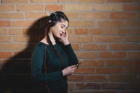 Woman in earphones listen music at brick wall in dark roomの写真素材