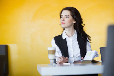 Young woman in white shirt drinking latte in yellow cafeの写真素材