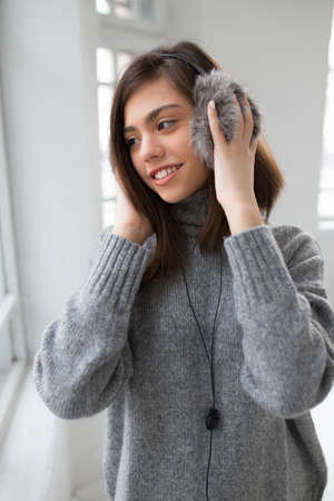 Teen girl with fluffy headphones listen music in white roomの写真素材