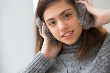 Teen girl with fluffy headphones listen music in white roomの写真素材