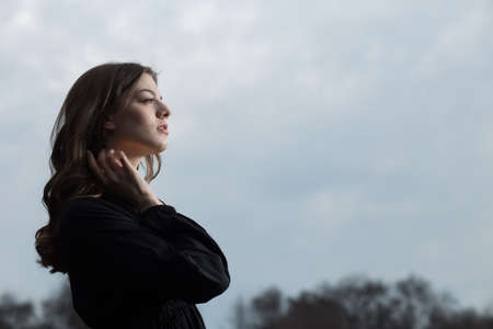 Beautiful woman in black dress against sullen sky background