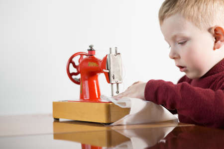 Little boy sew the fabric on the sewing machine - white backgroundの写真素材