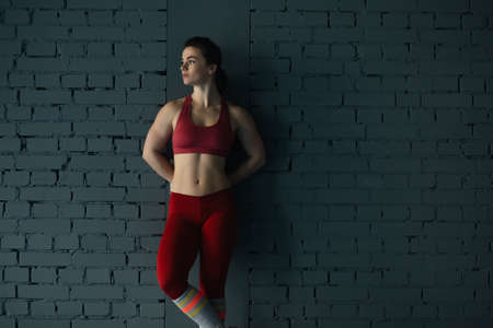 Sportswoman in red standing at brick wall in gymの写真素材