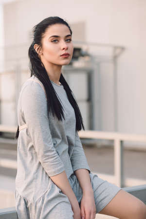 Stylish young woman sitting on roof and relaxation, evening city backgroundの写真素材