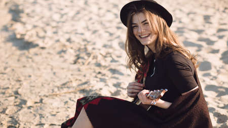 Happy young woman playing on ukulele at beach at summer holidays