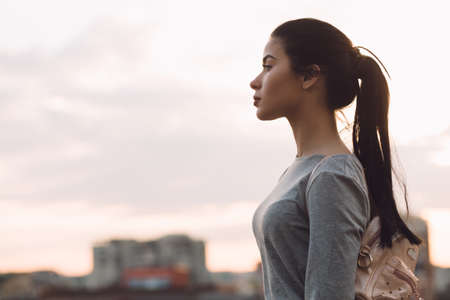 Stylish young woman standing on roof and relaxing, evening city backgroundの写真素材