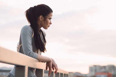 Stylish young woman standing on roof and relaxation, evening city backgroundの写真素材