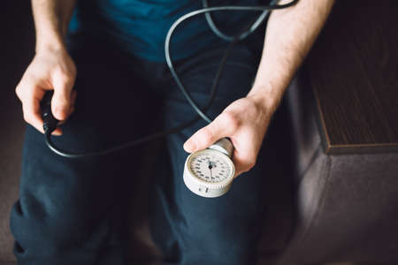 Man measuring blood pressure with tonometer himself at home sitting in armchairの写真素材