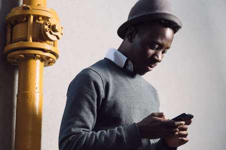 Portrait of african american man in hat using mobile phone near plumbing