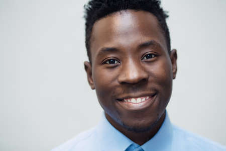 Classical portrait of smiling african american man in blue shirt at grey wall backgroundの写真素材
