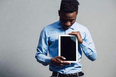 African american man in blue shirt using tablet PC at grey wall background