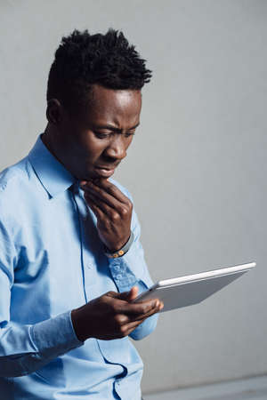 African american man looking to screen of the tablet PC at grey wall background