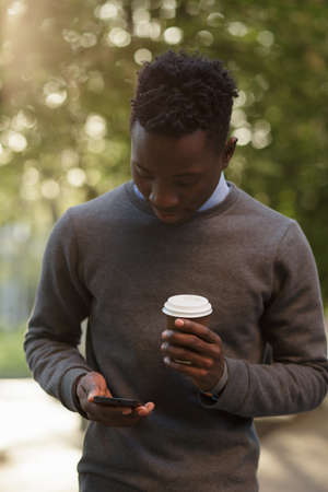 African american man walking to city street and typing text in smartphone