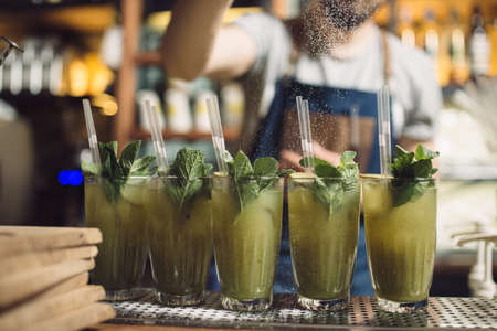 Young male bartender preparing an row of mochito at a bar counter, he pours the powderの写真素材