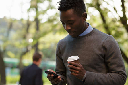 African american man walking to city street and typing text in smartphoneの写真素材