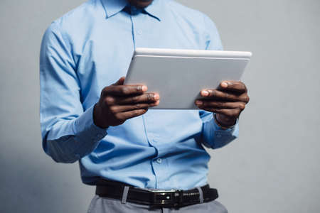 Black man in blue shirt using tablet PC at grey wall background - cropped shotの写真素材