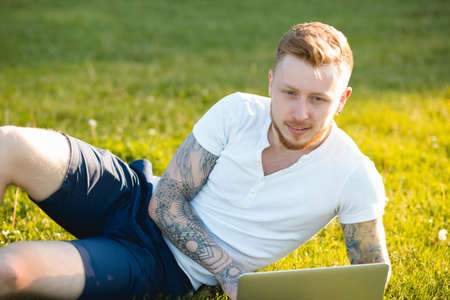 Young blogger sitting on grass and working with laptopの写真素材
