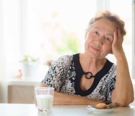 Happy senior woman looking at a camera as she sits in her homeの写真素材