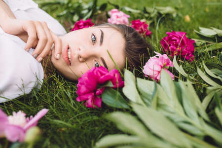 Woman lying on grass with flowers peonies around - creativeの写真素材