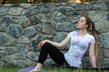Woman on a sportive mat sitting relaxing outdoor. Girl resting in park, nearby bottle of water after practicing yogaの写真素材