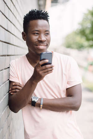 African american man standing near building in summer city and using his smartphone. Communication technology concept.の写真素材
