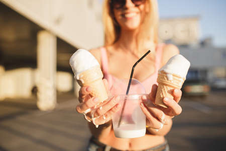 Sunny day, woman in city showing milk shake and ice creamの写真素材