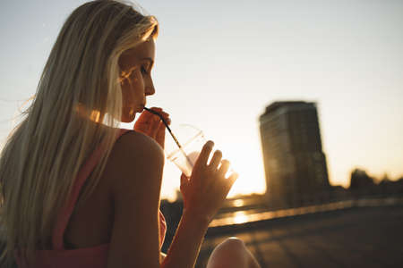 Woman drinking milk shake sitting in city sunset enjoying summer holidaysの写真素材