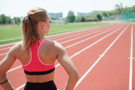 Young unrecognizable sporty woman athlete in sportswear ready to run on stadium track - back view