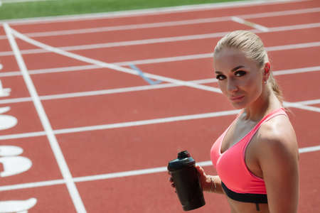 Young sporty woman athlete in sportswear drinking water or protein cocktail from shake on stadium trackの写真素材