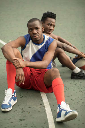Two african american man friends sitting on street basketball courtの写真素材