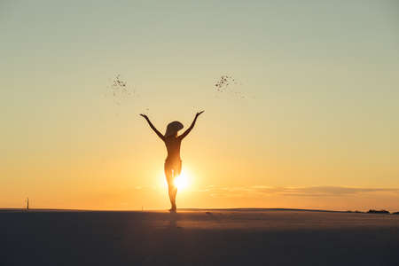 Silhouette of woman throws sand in gold desert at sunset