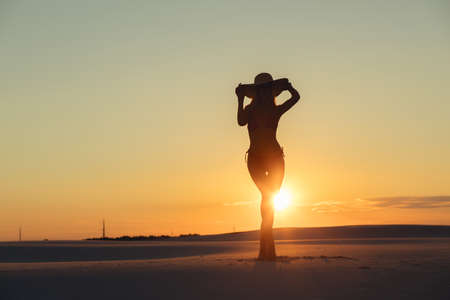 Silhouette of beautiful woman posing with hat in gold desert at sunsetの写真素材