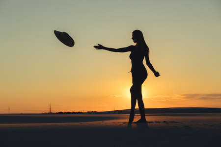 Silhouette of woman throws hat in gold desert at sunsetの写真素材
