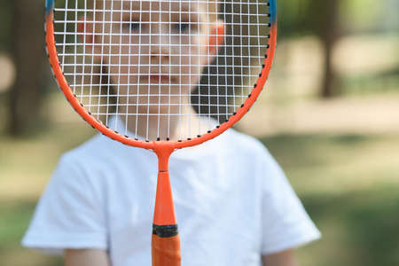 Portrait of little boy behind a badminton racket in a pine forest, active rest at a nature