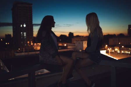 Silhouette of two young girl friends looks to evening dusk city scape