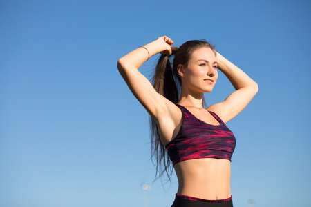 Young happy sportswoman in sportswear tie the hair ponytail isolated on blue sky background.の写真素材