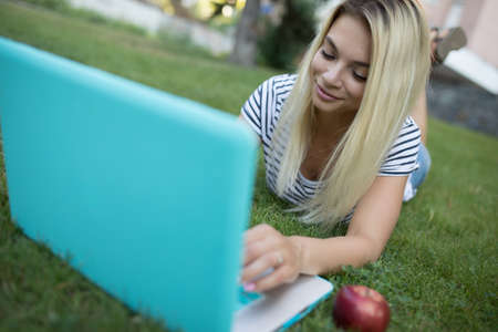 Pretty woman  working with her laptop outdoor lying on grass in parkの写真素材