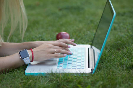 Closeup of woman hands typing text on keyboard of her laptop outdoor lying on grass in parkの写真素材