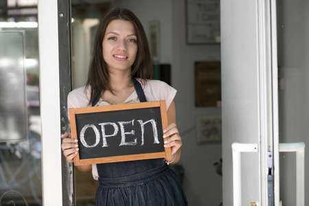 Portrait of young woman holding up an open signboard in her store
