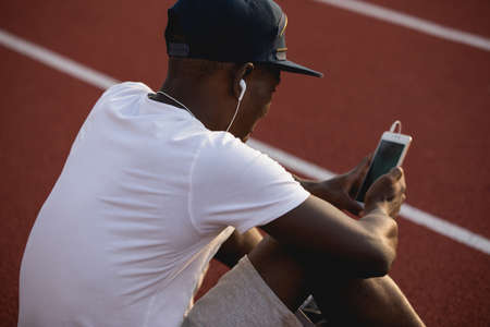 African american male sportsman sit on stadium track and listen music after hard workout