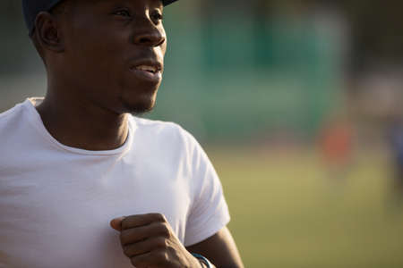African male sportsman in a cap running on stadium track, he trains enduranceの写真素材