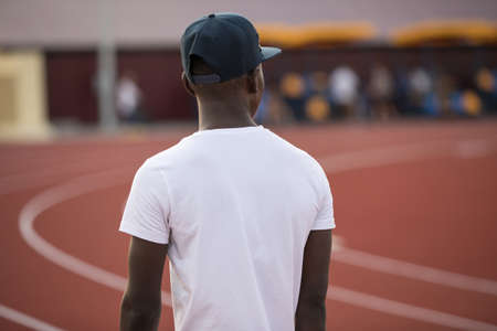 Sportsman in a cap on stadium, african male workout outside, rear viewの写真素材