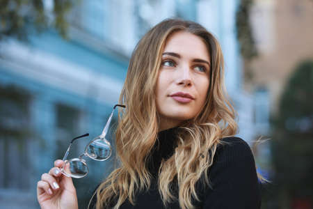 Myopia, portrait of young woman student holding eyeglasses for good vision, blue building backgroundの写真素材