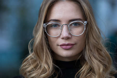 Myopia, close-up portrait of young woman student in eyeglasses for good vision look at camera, blue...