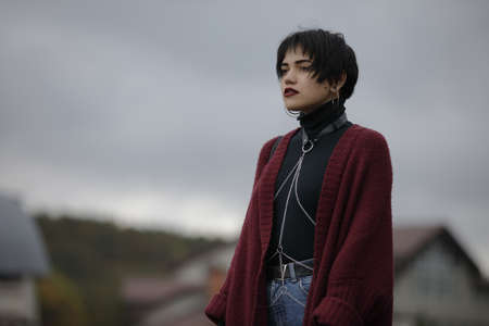 Unconventional woman portrait in marsala color cardigan with black leather sword belt at overcast sky backgroundの写真素材