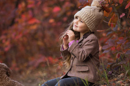 Little girl enjoying autumn day sitting on nature playing sound with stick, virtual fluteの写真素材