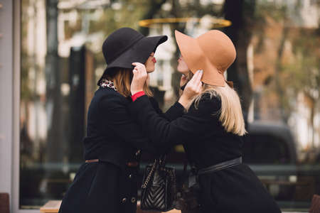 Fashionable women friends in hat make kiss gesture to each otherの写真素材