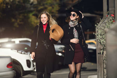 Fashionable women friends in hats walking at city