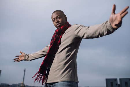 Brutal african american man with scarf raised hands in city sky background